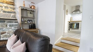 A modern living room with a leather sofa, a stone wall, a coffee menu sign, and a kitchen with white cabinets and a wooden staircase. - The Toll House (Dolgellau)