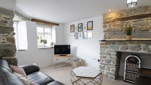 A living room with a stone fireplace, a television on a wooden stand, a black leather sofa, and a marble coffee table. - The Toll House (Dolgellau)