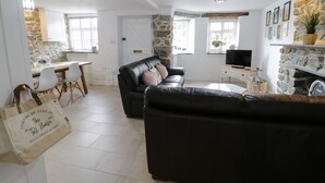 A spacious living area with a black leather sofa, a dining table with chairs, a stone wall, and a television. - The Toll House (Dolgellau)