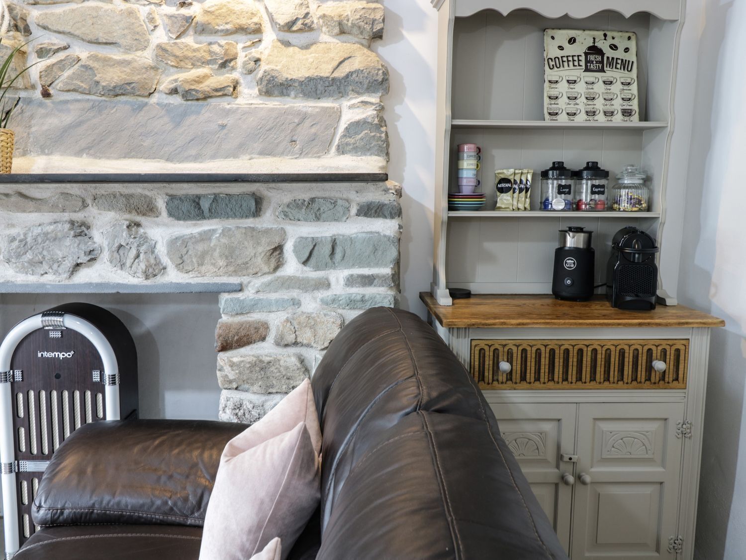 Un salon chaleureux avec un mur en pierre, une machine à café et une étagère remplie de tasses à café.