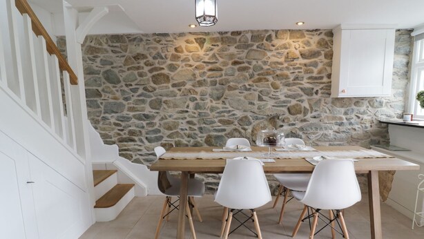 A dining area with a stone wall, white chairs, and a wooden table. - The Toll House (Dolgellau)