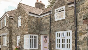 A stone building with multiple windows and a door, featuring a small porch with potted plants. - The Toll House (Dolgellau)