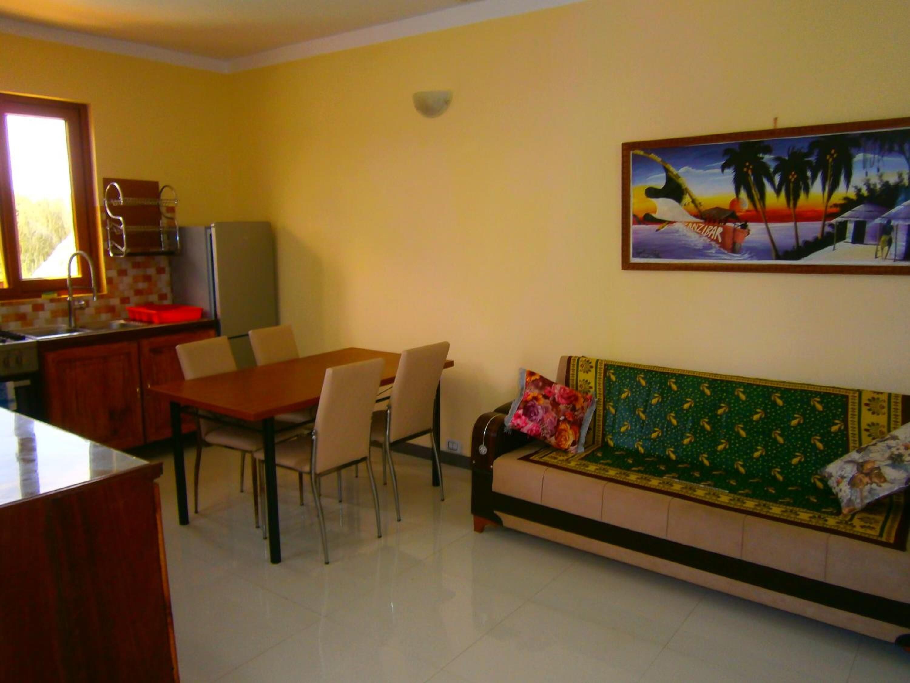 Un comedor con una mesa y sillas, una kitchenette, un sofá con cojines y un cuadro en la pared.