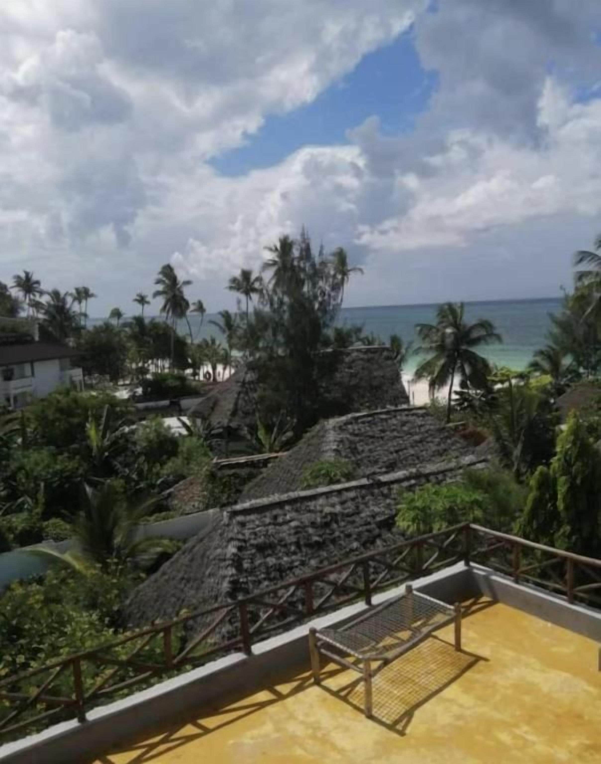 Un resort tropical con una estructura de techo de paja, un área de piscina y vista al océano.