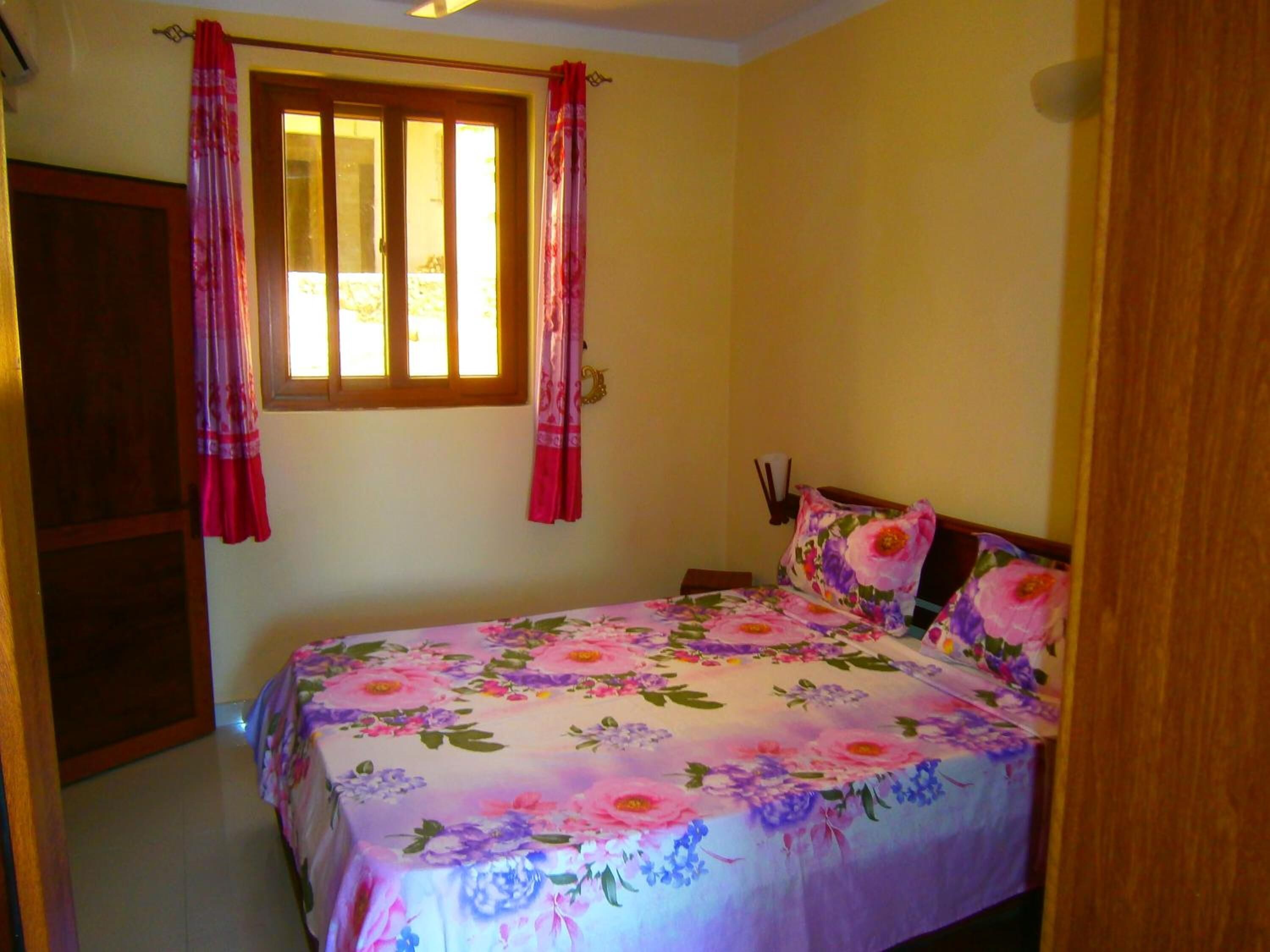 A bedroom with a bed, curtains, a window, and a door.