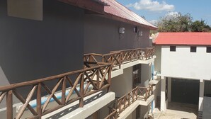 Un edificio de varios pisos con techo rojo, balcones con barandillas de madera y un estacionamiento con un coche.