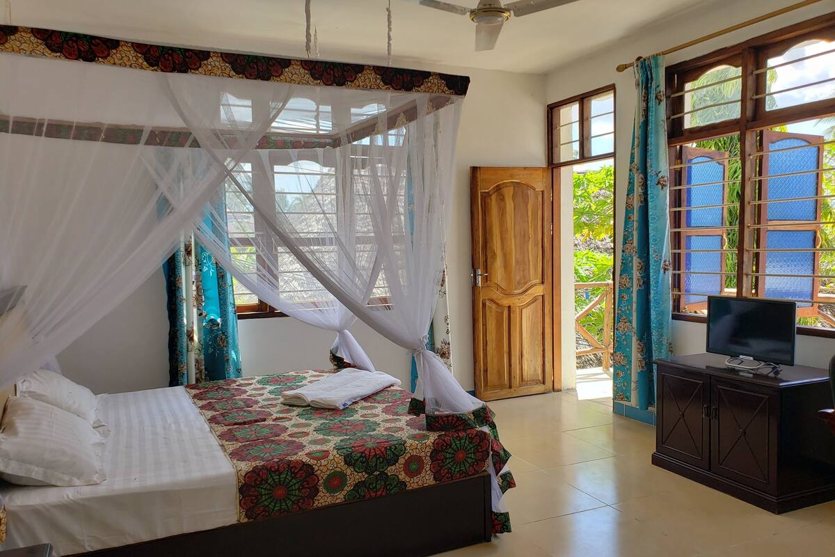 A bedroom with a bed, a TV, and a window with curtains.