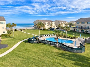 A resort with a pool, palm trees, and a view of the ocean.