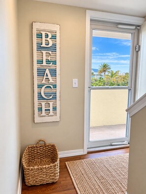 A hallway with a wooden sign reading 'BEACH' on the wall, a woven basket, and a textured rug on the floor.