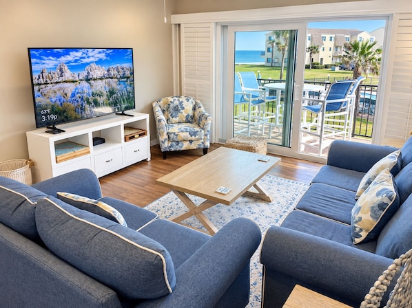 A living room with a television, sofa, armchair, and a view of the outdoors.