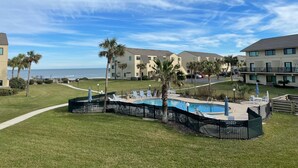 Ett poolområde med solstolar och palmer, omgivet av bostadshus med utsikt över havet.