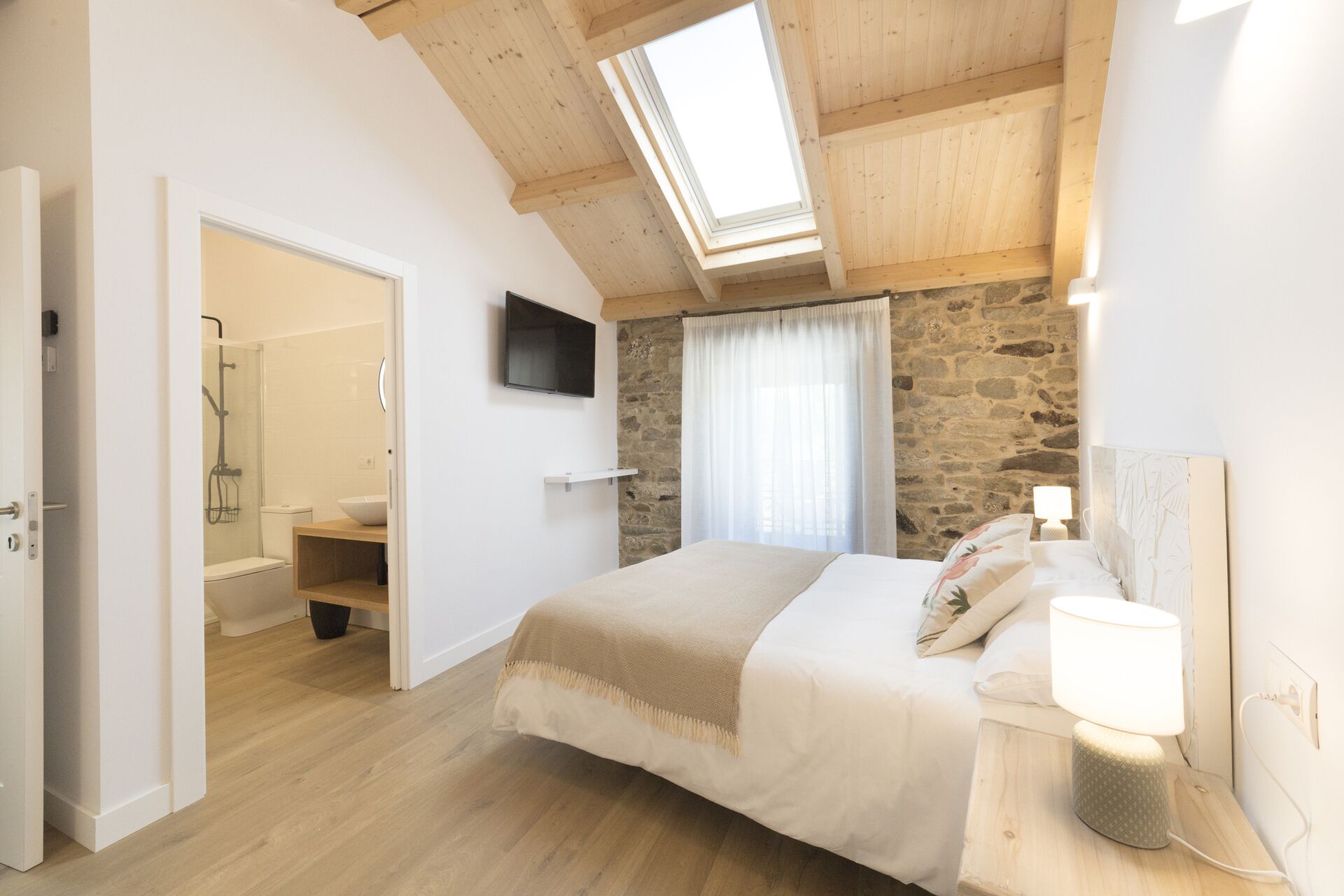 Une chambre avec une lucarne, un mur en pierre, un lit avec une lampe et un espace douche.
