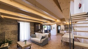 A spacious living area with a stone wall, wooden beams, a sofa, a dining table, and a staircase. - Landras de Compostela (Santiago de Compostela)