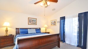 Quarto com cama de madeira, duas mesas de cabeceira com luminárias, um ventilador de teto e duas imagens emolduradas na parede.