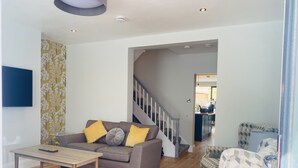 Un salon comprenant un canapé, des fauteuils, une table basse et un escalier menant à une autre pièce.
