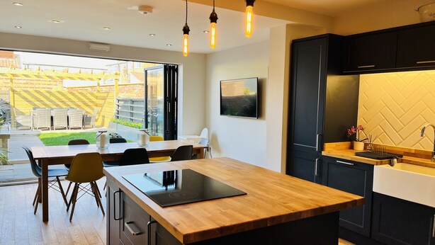 Une cuisine moderne avec un îlot central en bois, des meubles de rangement noirs et une grande fenêtre donnant sur un jardin.