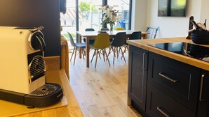 Une cuisine moderne équipée d’une machine à café, de meubles en bois, d’un coin repas avec des chaises et d’une grande fenêtre.