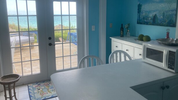 A room with a view of the ocean through a glass door, a white dining table, a white cabinet, and a painting on the wall.