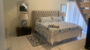 A bedroom with a large bed, a nightstand, a lamp, a mirror, and a staircase.