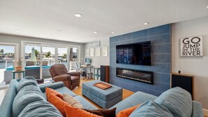 Een moderne woonkamer met een grote televisie, comfortabele zithoek en uitzicht op buiten.