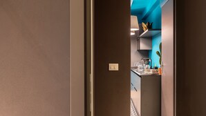 A narrow hallway leading to a kitchen with a blue accent wall and modern appliances. - Apartment (Siracusa)
