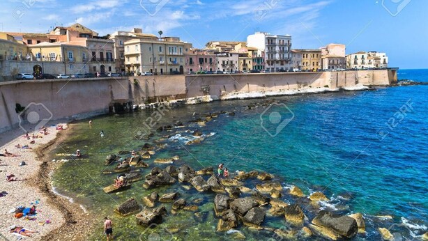 A coastal town with buildings along the sea, clear waters, and rocky areas. - Apartment (Siracusa)