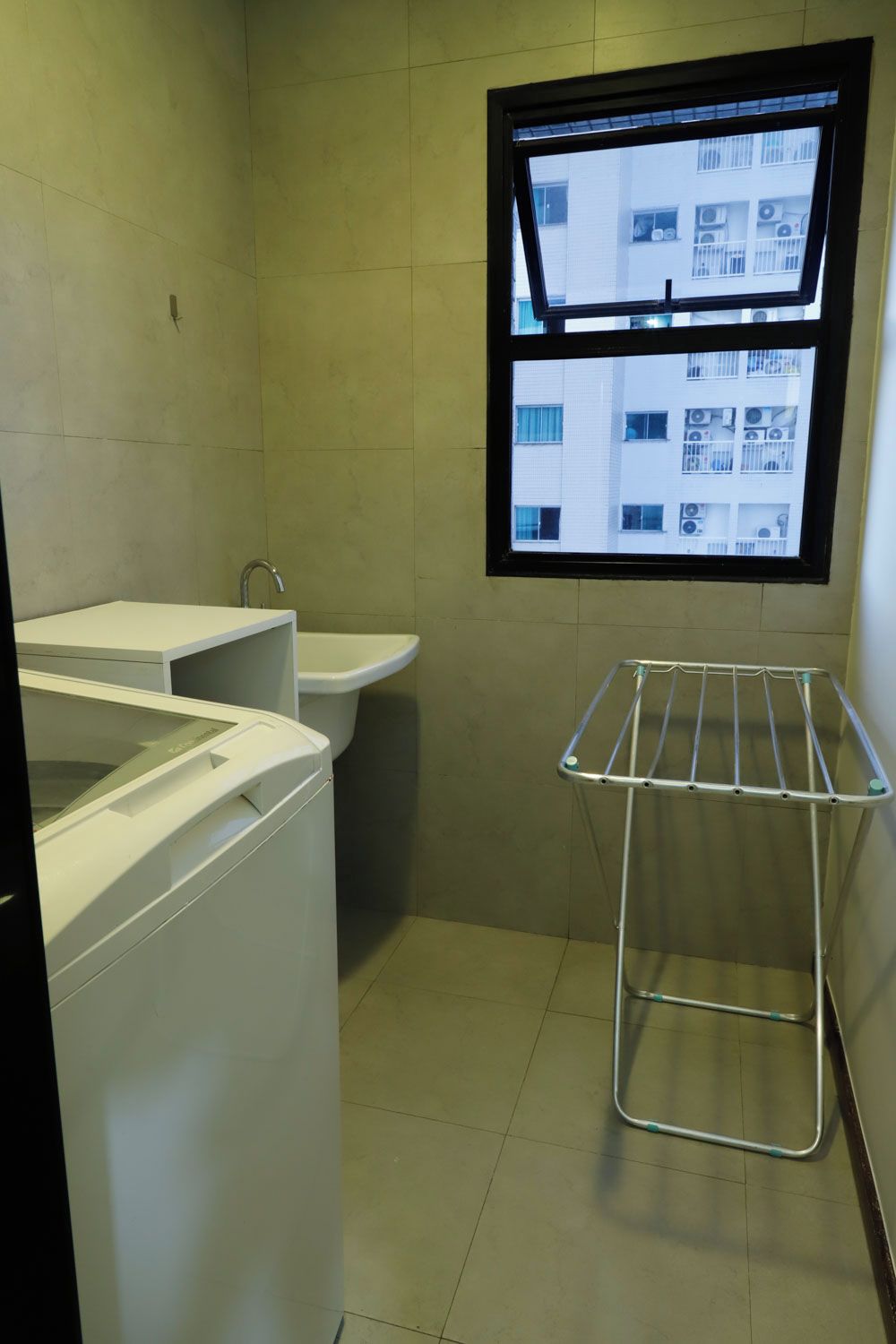 A small laundry room with a washing machine, a sink, and a drying rack.