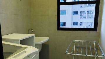 A small laundry room with a washing machine, a sink, and a drying rack.
