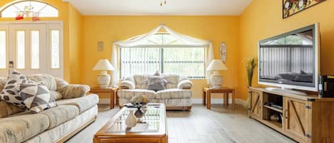 A living room with a sofa, two armchairs, a coffee table, a TV, and a ceiling fan.