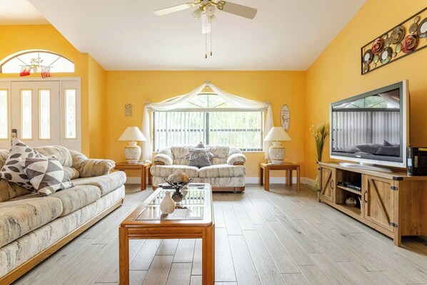 A living room with a sofa, two armchairs, a coffee table, a TV, and a ceiling fan.
