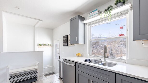 Une cuisine moderne avec des meubles gris, un plan de travail blanc et une fenêtre donnant sur un paysage enneigé.
