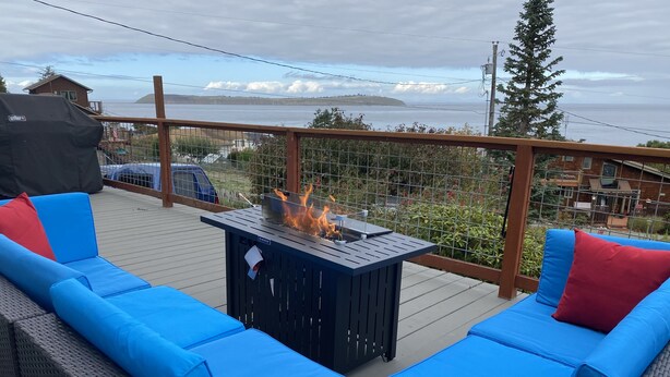 An outdoor deck with blue cushioned seating, a fire feature, and a view of the ocean. - Amazing views (Sequim)