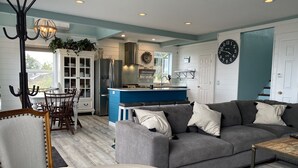 A modern kitchen with a blue island, a gray sofa, and a dining area with wooden chairs. - Amazing views (Sequim)