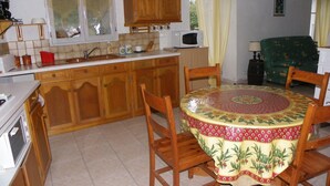 A kitchen with wooden cabinets, a microwave, and a dining table with chairs. - Studio (Canari)