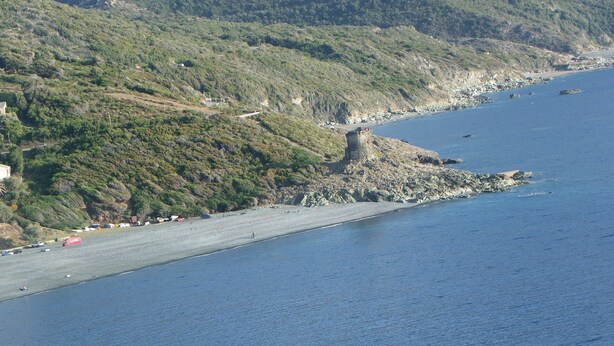 A coastal area with a rocky shoreline, a beach, and a hilly landscape in the background. - Studio (Canari)
