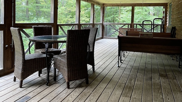 Una terraza cubierta de madera con mobiliario de mimbre y una mesa de vidrio, con vista a un área boscosa.