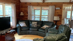 Un interior acogedor de cabaña de madera con un sofá seccional, un televisor de pantalla plana y una decoración rústica.