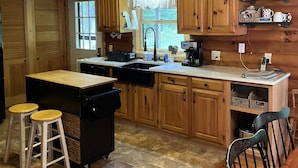 Cocina de estilo rústico tipo cabaña, con armarios de madera, una isla central, taburetes y una mesa de comedor.