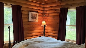 Un dormitorio de cabaña de madera con cama, mesita de noche, lámpara y un cuadro en la pared.