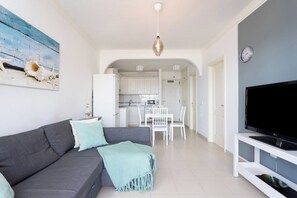 Uma sala de estar moderna com um sofá cinzento, uma televisão de tela plana e um espaço de jantar com mobiliário branco.