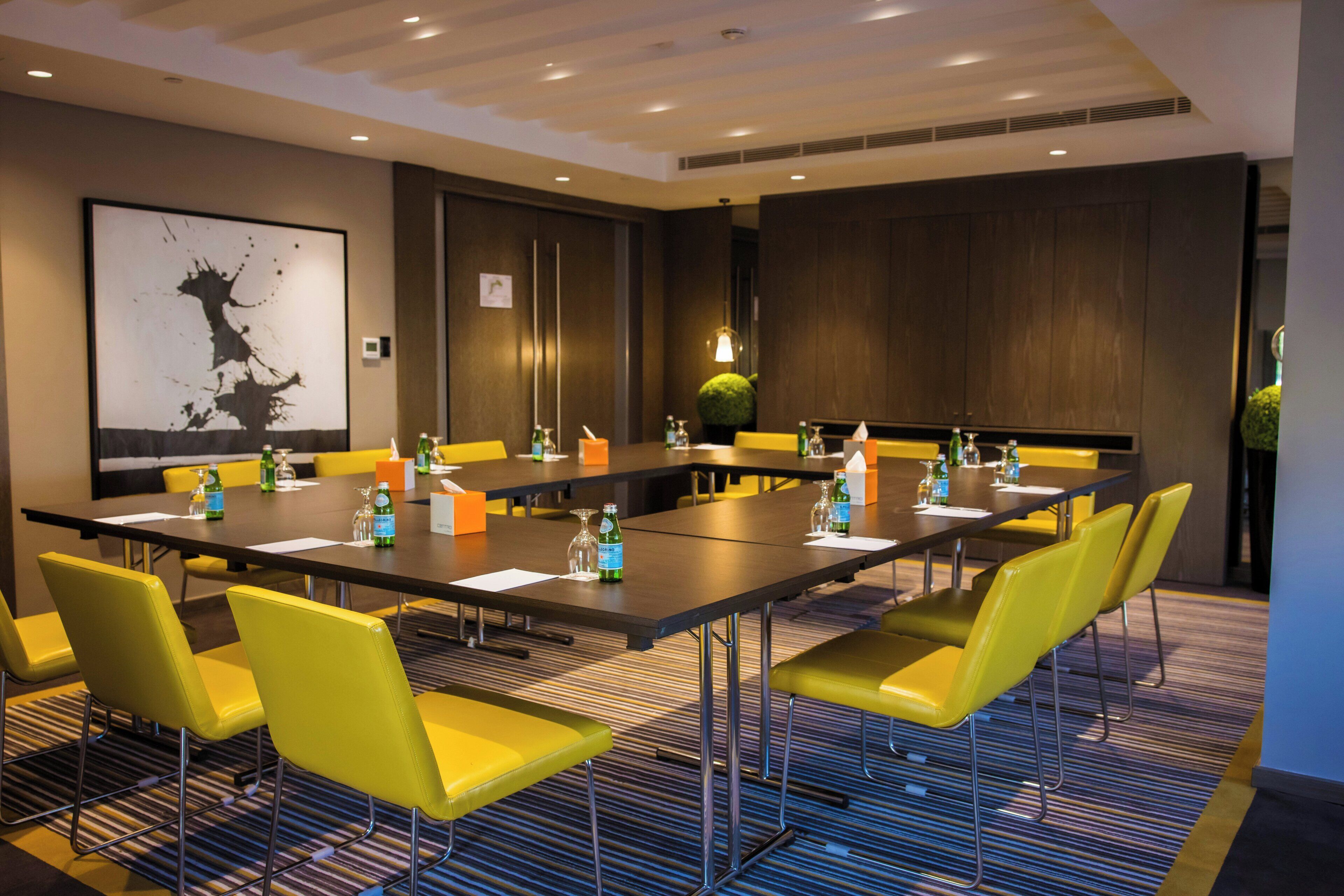 A conference room with a long table, yellow chairs, and a large abstract painting on the wall.