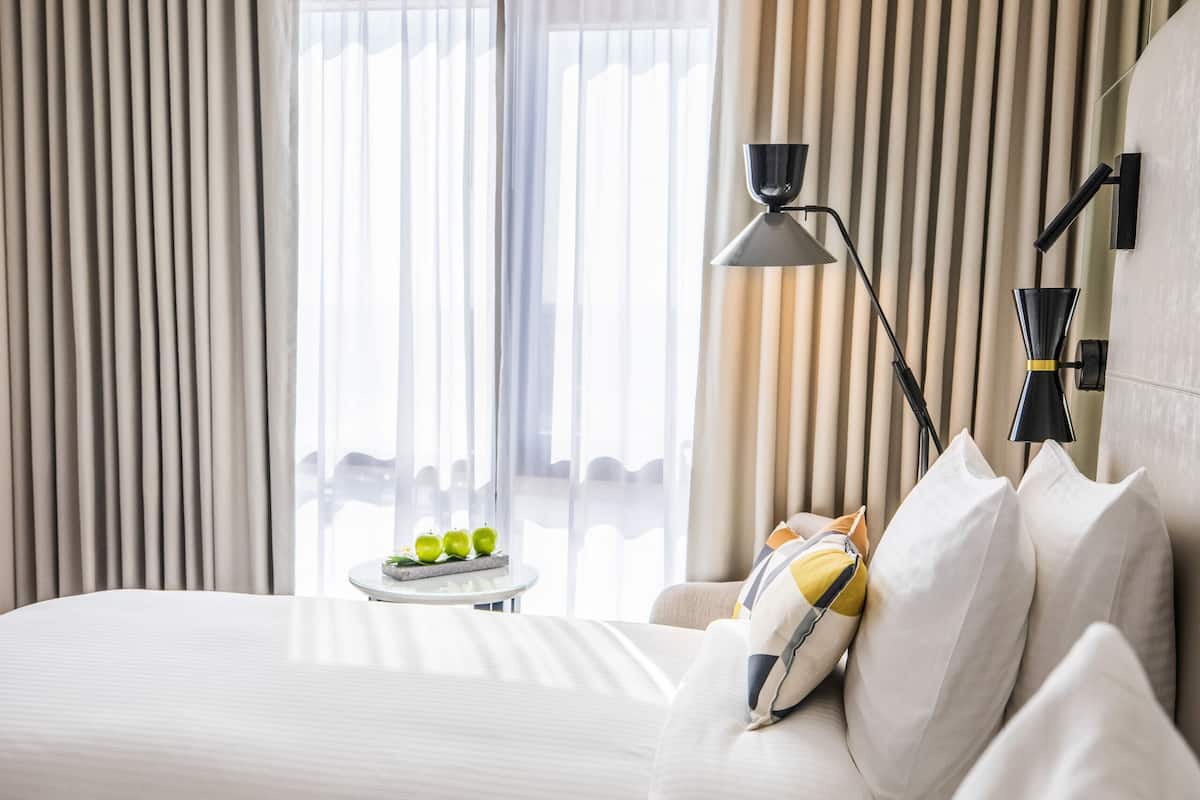 Une chambre d’hôtel moderne avec deux lits, une table de chevet avec une lampe et une vue sur la ville grâce à de grandes fenêtres.