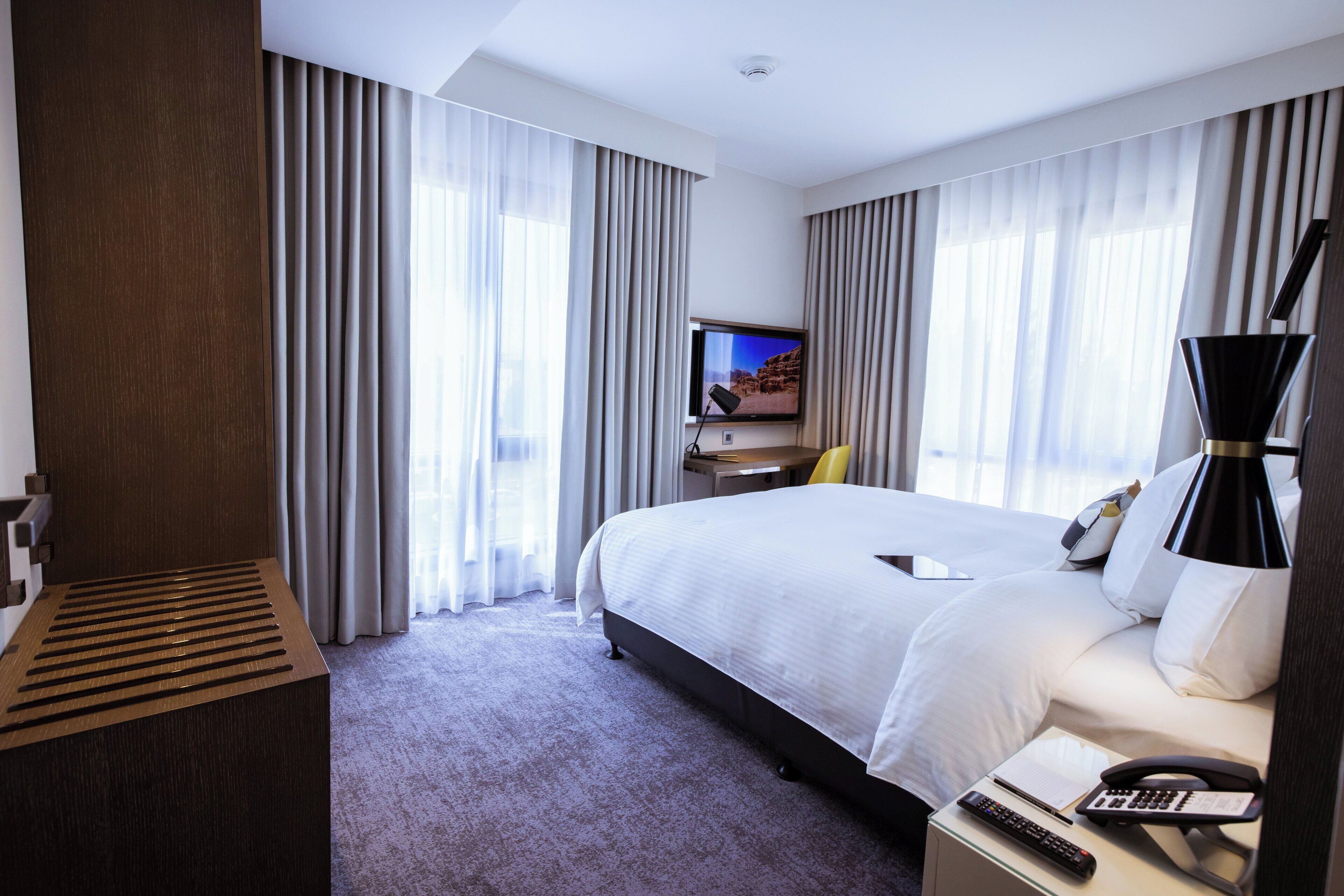 Una habitación de hotel moderna con una cama grande, un escritorio con ordenador, un televisor y una lámpara.