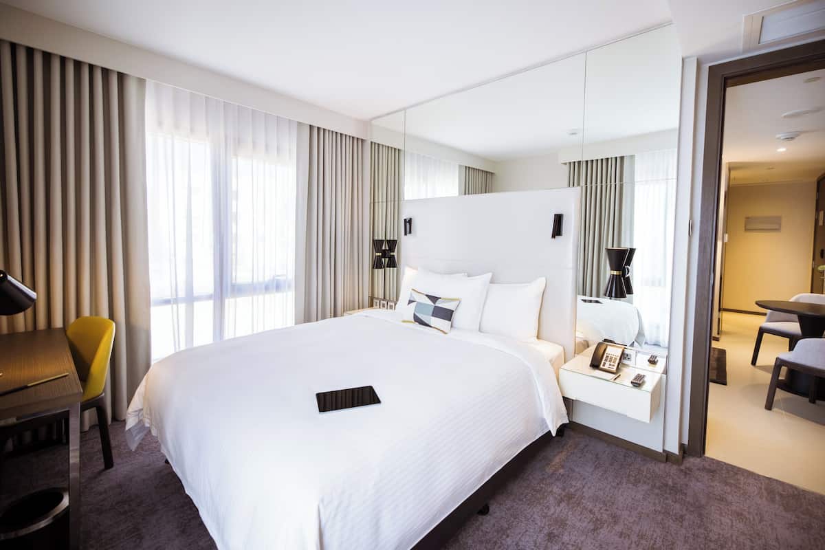 Une chambre d’hôtel avec un grand lit, une table de chevet avec un téléphone, un bureau avec une chaise et un miroir.