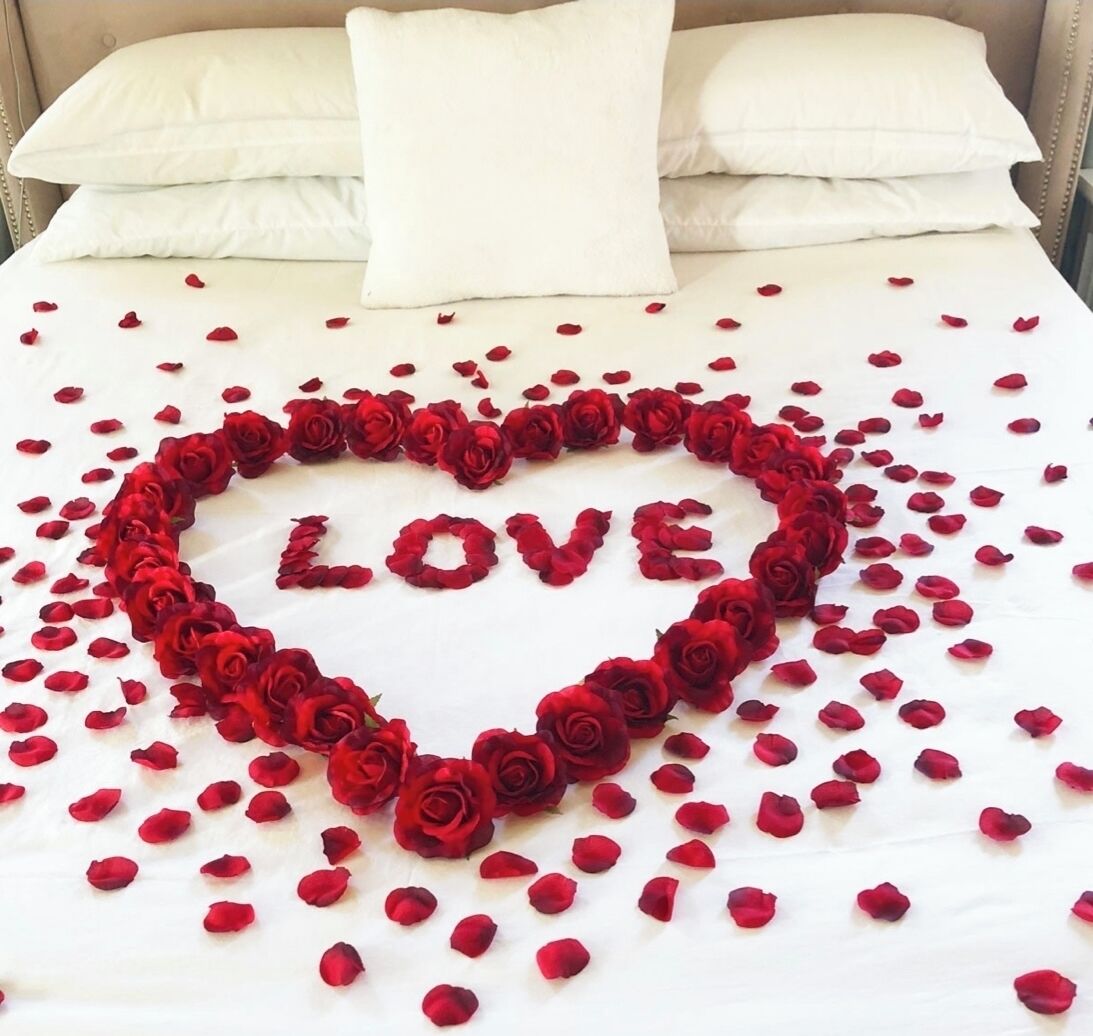 En seng med en hjerteformet sammensætning af røde roser, der staver "LOVE", og spredte rosenblade.