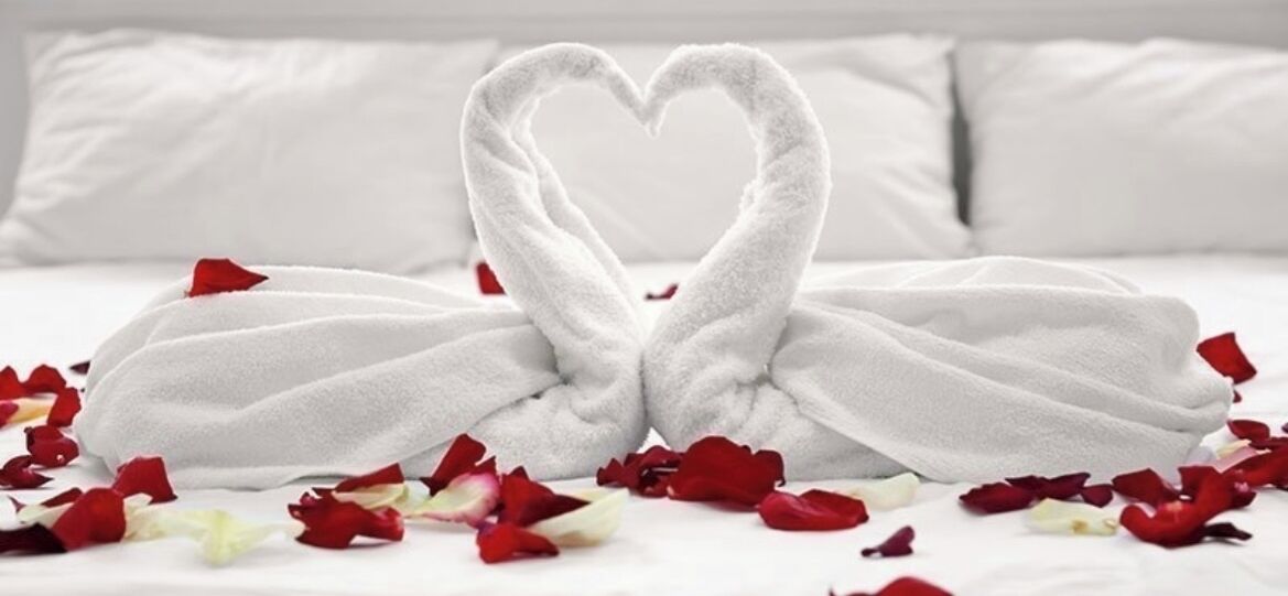 A bed with white linens and a heart-shaped towel arrangement.
