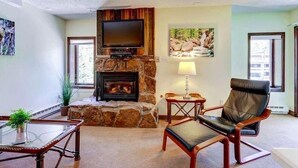 A living room with a stone fireplace, a flat-screen TV, a comfortable leather chair, and a glass coffee table. - Vail Run Resort for Christmas Break (Vail)