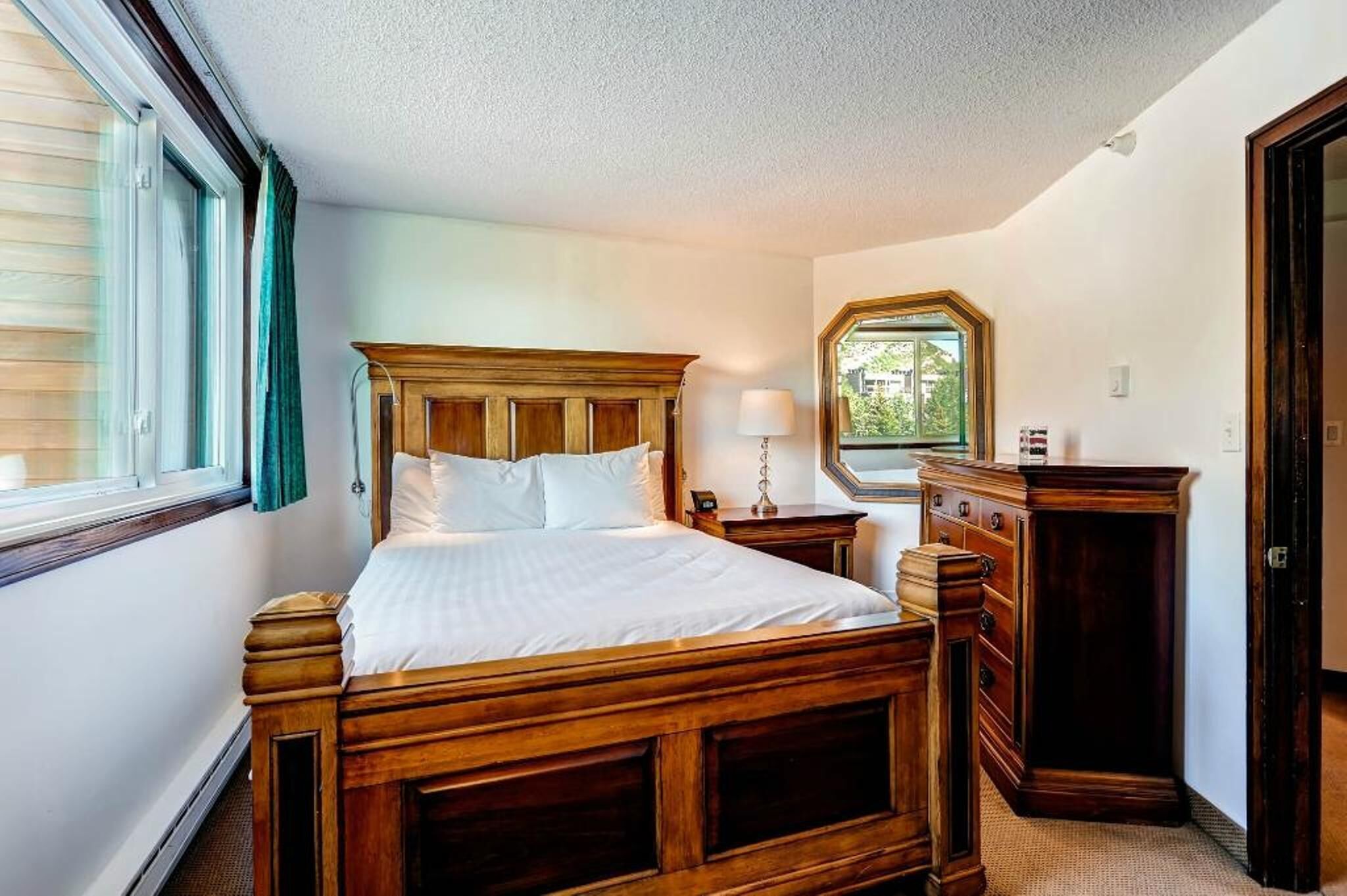 A bedroom with a wooden bed, a dresser, a nightstand, and a window with curtains.