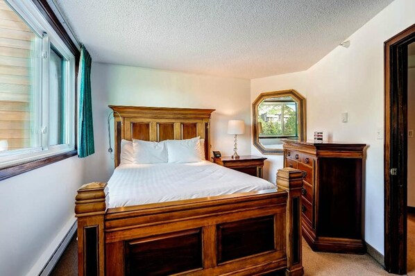 A bedroom with a wooden bed, a dresser, a nightstand, and a window with curtains.