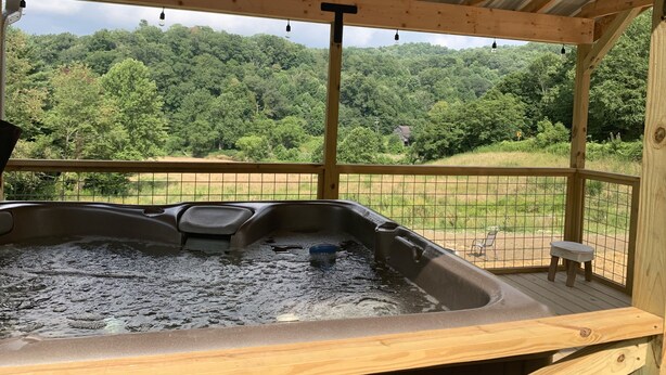Un bain à remous installé sous une terrasse en bois, offrant une vue sur une colline boisée.